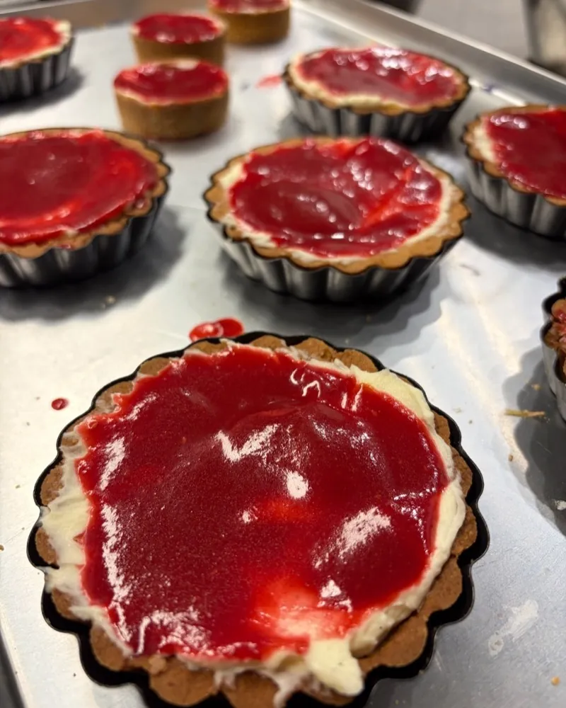 Tartlets with pale cream and a glossy red raspberry coulis on a tray.