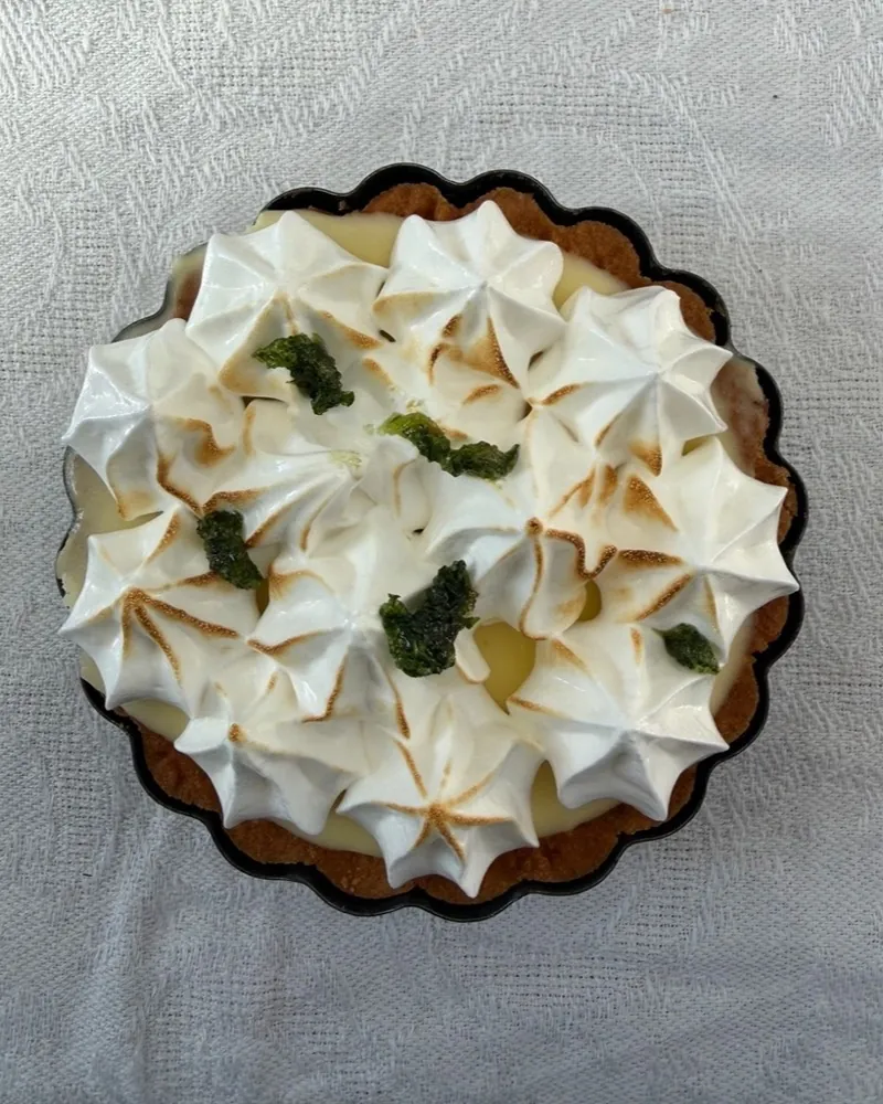 Tarte au citron with torched meringue and small green pieces, seen from above.