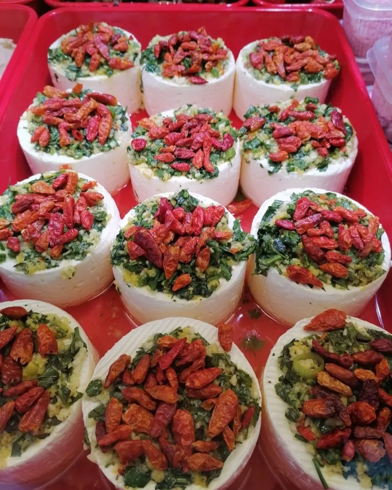 Rotes Tablett mit Frischkäse-Röllchen bei Naim's Feinkost auf dem Bötzowmarkt, belegt mit getrockneten Tomaten und Kräutern, dahinter Oliven.