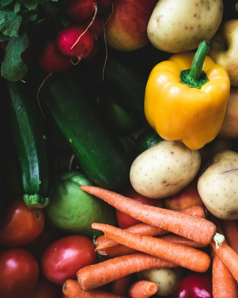 Freshly harvested vegetables packed close together: courgettes, radishes, yellow peppers, potatoes, carrots and tomatoes.