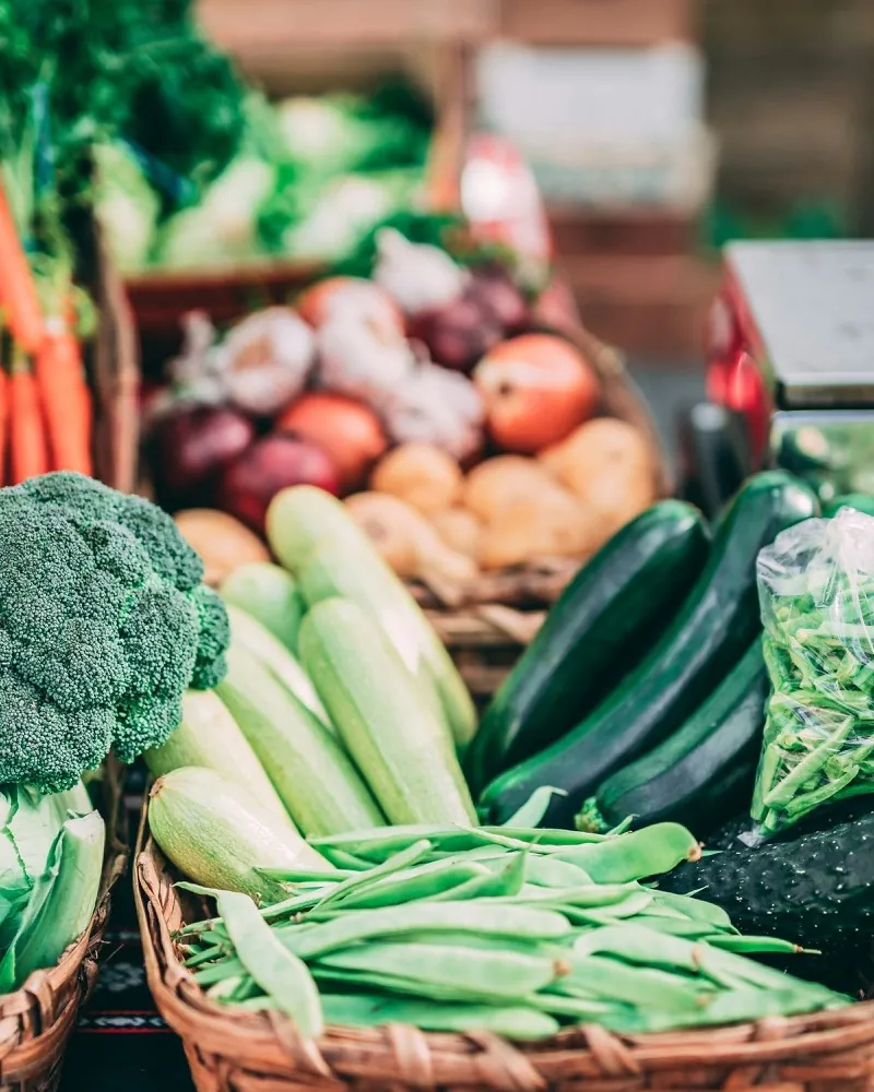 Baskets of beans, courgettes and broccoli at a market stall, a scale behind them.