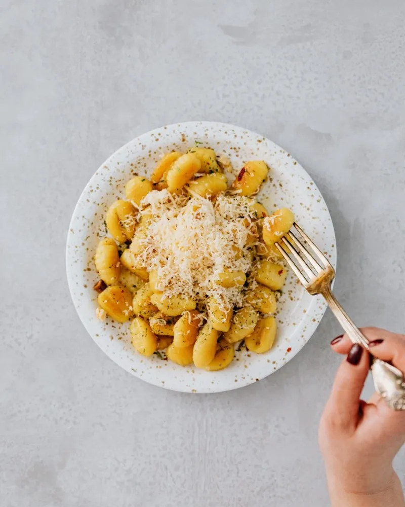 A plate of gnocchi with grated cheese, a fork held beside it.