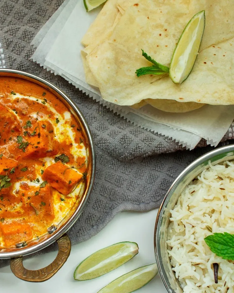 A curry in a metal bowl, with flatbread and rice with mint beside it.