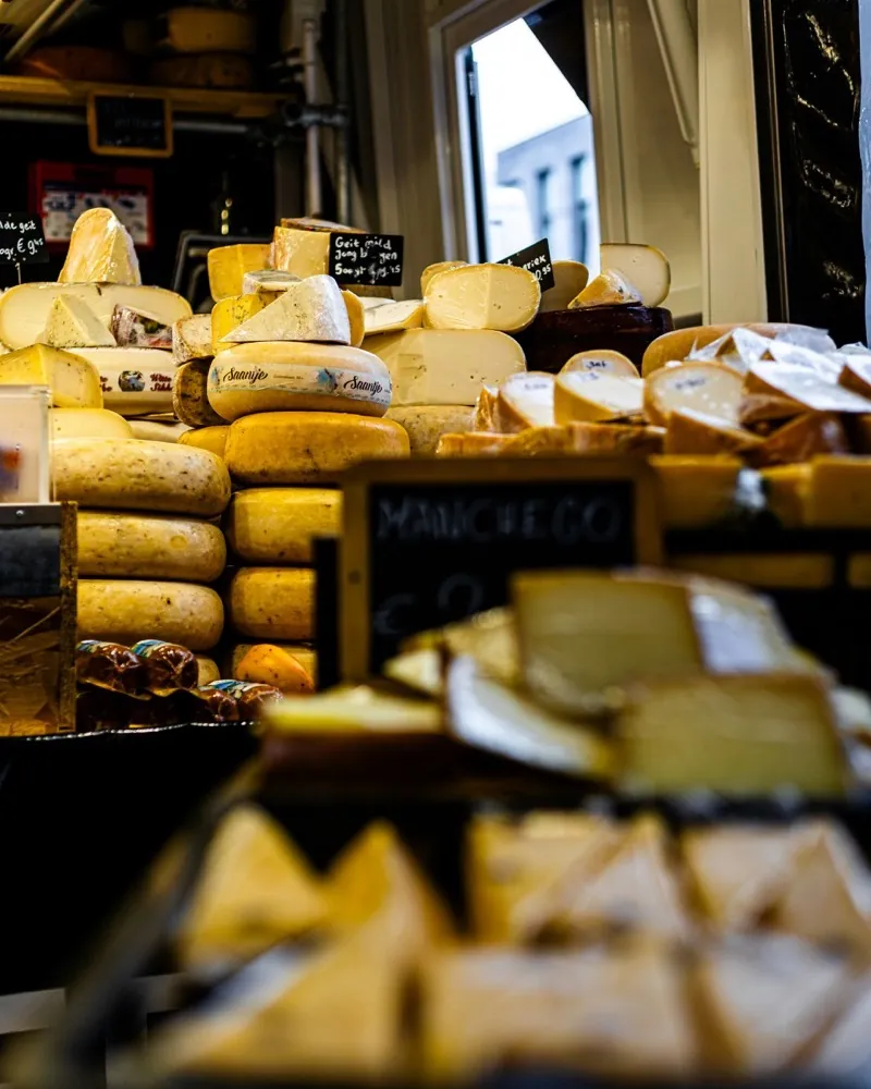 Stacked wheels of cheese in a market van, a price board in front of them.