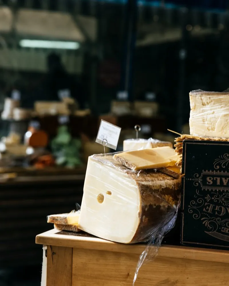 A large piece of cheese on a wooden counter, the dim market stall behind it.