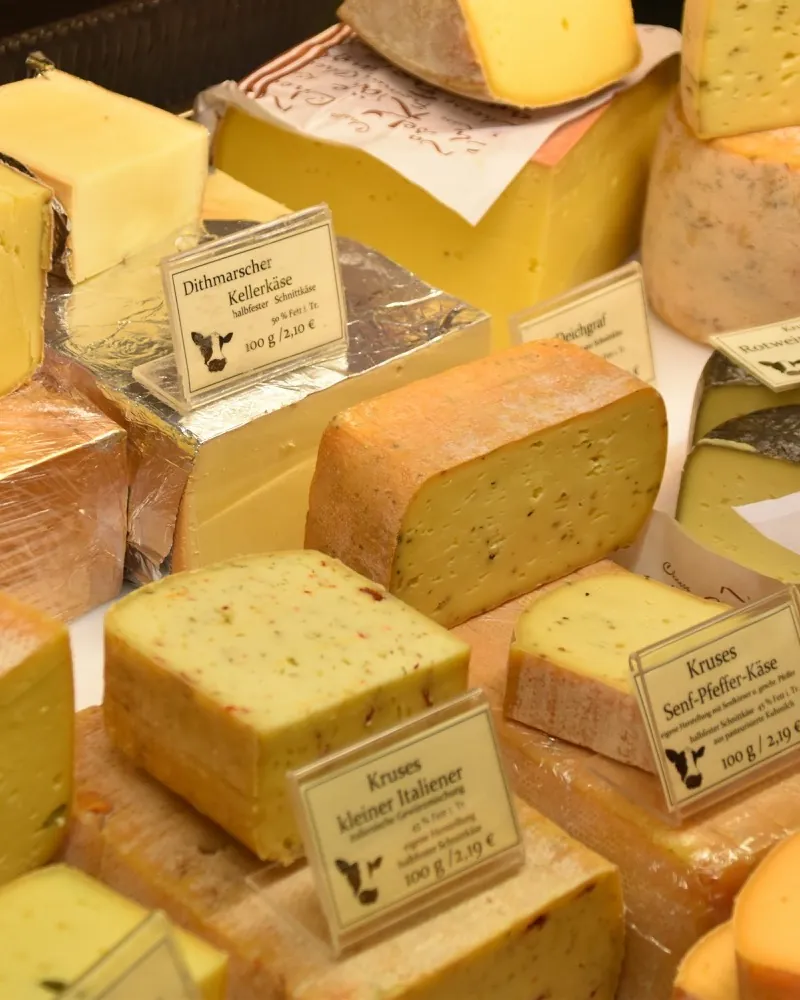 Cheese counter with cut wheels and labels: Dithmarscher Kellerkäse, Kruses Senf-Pfeffer-Käse.