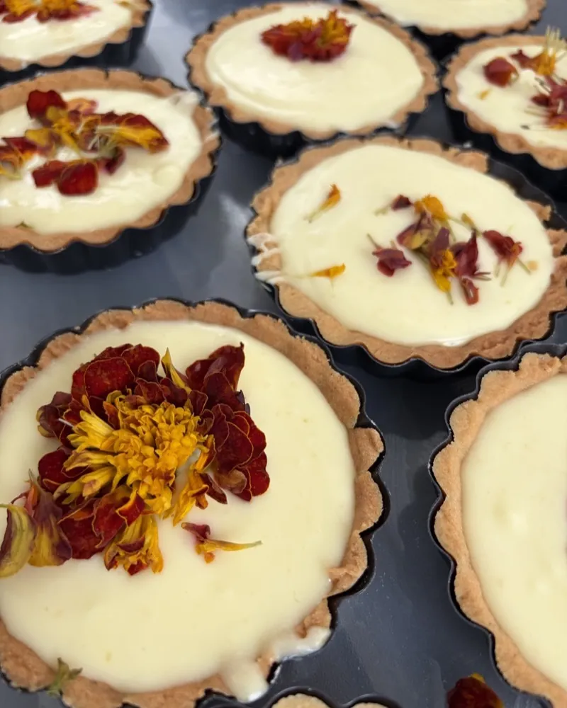 Tartlets with pale cream, decorated with edible flowers in yellow and red.