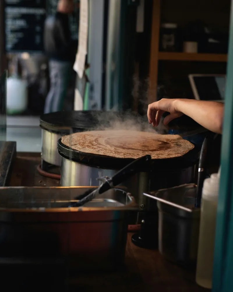 A crêpe cooking on the round hotplate of a market stall, steam rising above it.